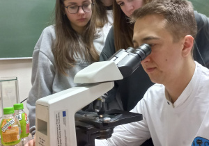 Pan profesor oglądający preparat pod mikroskopem wraz z uczniami